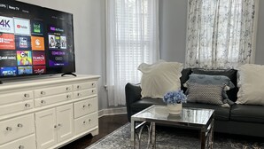 Ein modernes Wohnzimmer mit einem Flachbildfernseher, einem Glastisch, einem dunklen Sofa und einer weißen Kommode.