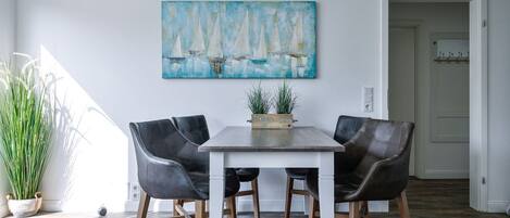 A dining area with a table, four chairs, a painting, and a potted plant.