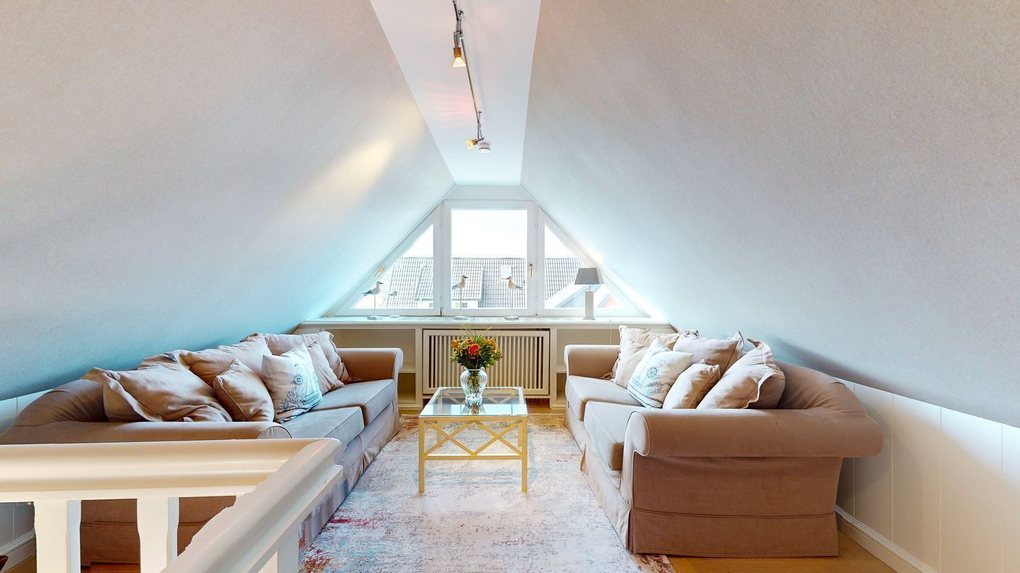 A loft-style room with two beige sofas, a glass coffee table, and a large window providing a view of the cityscape.