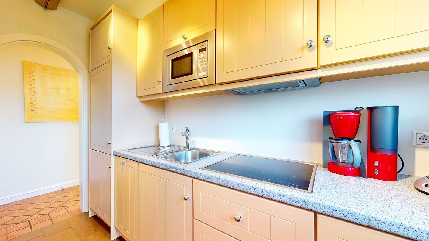 A kitchen with a microwave, sink, and red coffee maker.