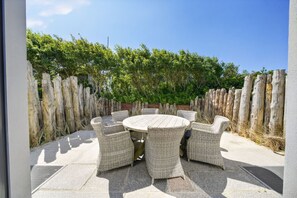 A round outdoor table with wicker chairs, surrounded by a wooden fence and greenery.