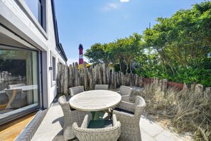 A patio with a round table and wicker chairs, a wooden fence, and a lighthouse in the background.