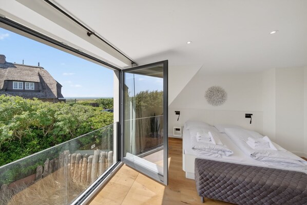 A modern bedroom with a large glass door leading to a balcony, a bed with white linens, and a decorative wall piece.