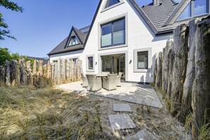 Ein modernes Haus mit weißer Fassade, einem Holzzaun und einer Terrasse mit Gartenmöbeln.