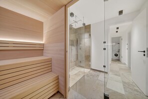 A modern bathroom with a wooden bench, a glass shower enclosure, and a laundry area visible through an open door.