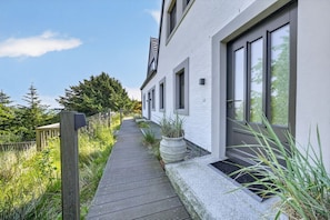 A pathway leading to a modern building with a white exterior, large windows, and a wooden fence.