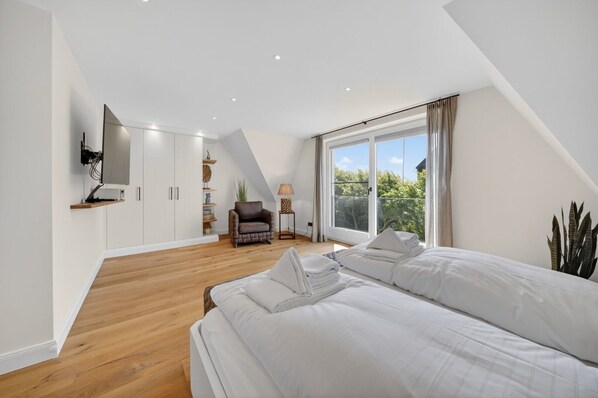 A bedroom with a large bed, a chair, a TV mounted on the wall, and a window with curtains.