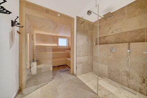 A modern bathroom with a glass-enclosed shower, wooden flooring, and a visible sauna area.