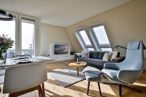 A modern living room with a dining area, a sofa, a TV, and skylights.