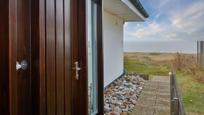 Eine Holztür, die zu einem Gebäude mit einem Steinweg und Blick auf das Meer führt.