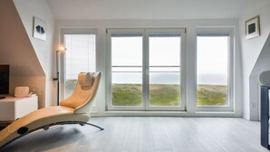 Ein modernes Zimmer mit einem gebogenen Sessel, einem Schreibtisch mit einem Laptop und großen Fenstern mit Meerblick.