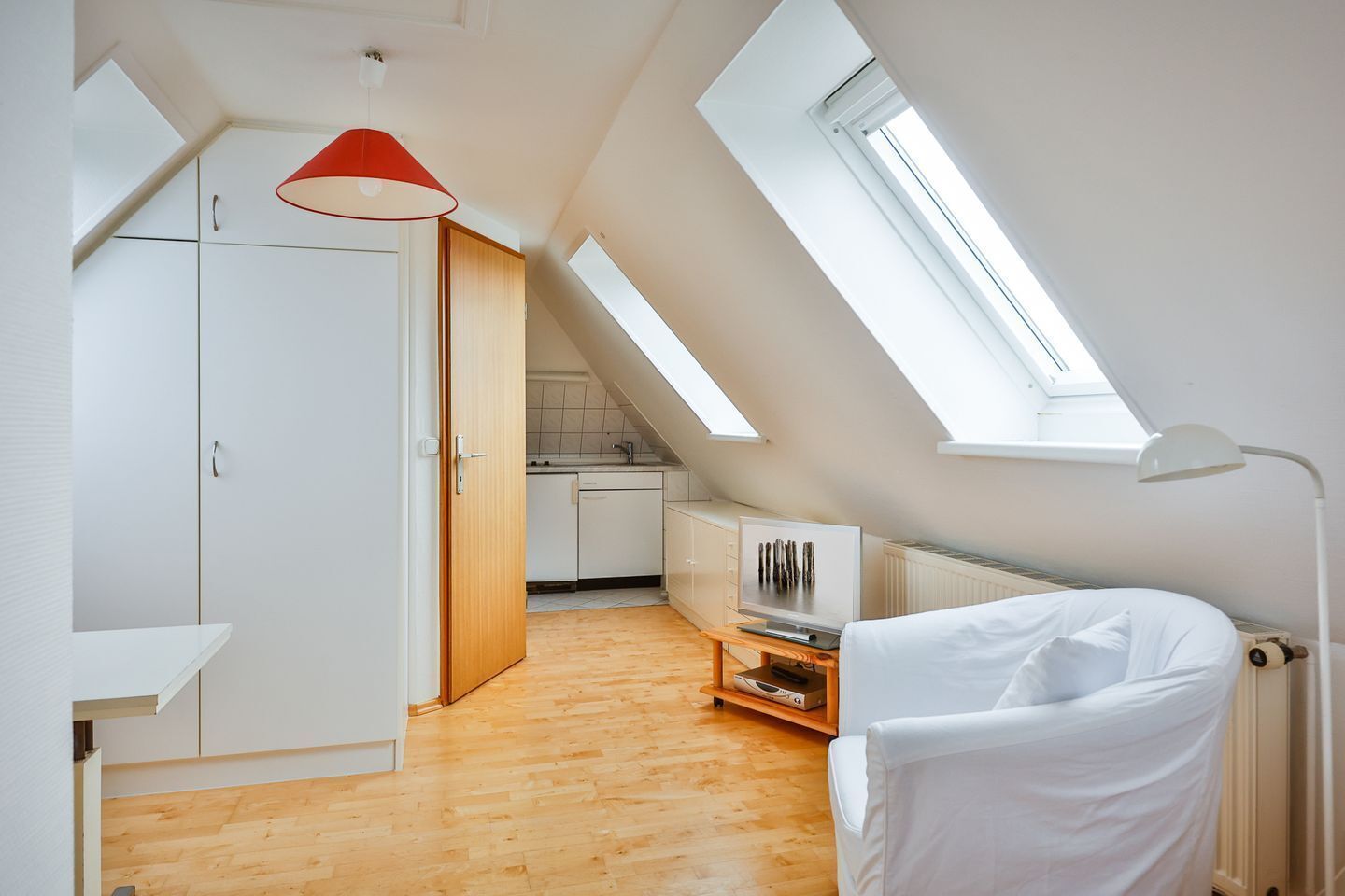 Un dormitorio estilo loft moderno con tragaluces, piso de madera, cama blanca y televisor sobre un mueble de madera.