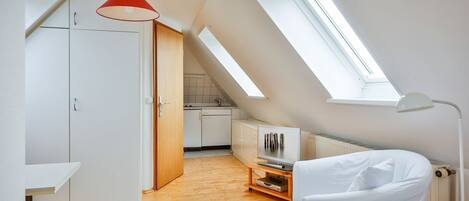 Un dormitorio estilo loft moderno con tragaluces, piso de madera, cama blanca y televisor sobre un mueble de madera.