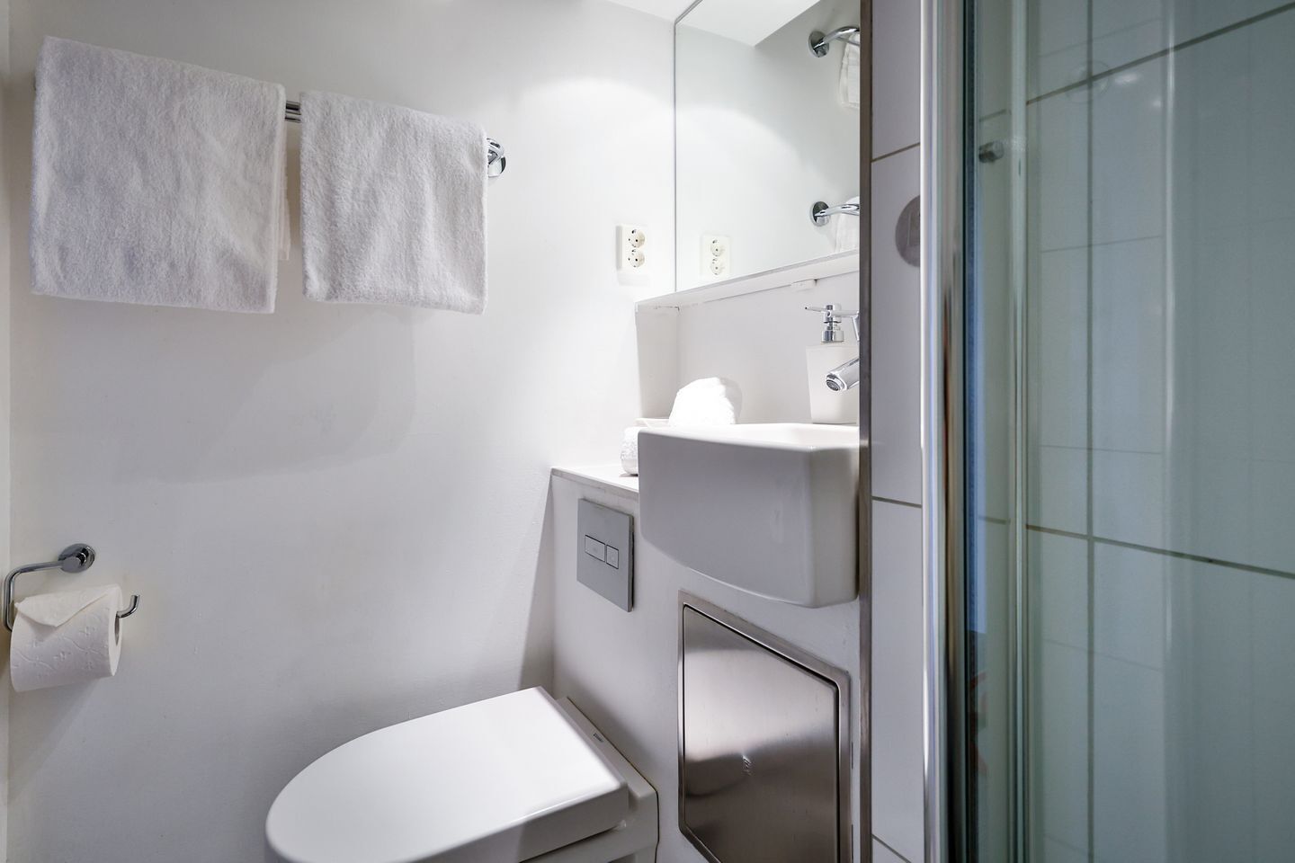 Een moderne badkamer met toilet, wastafel en douche. Twee witte handdoeken hangen aan haken.