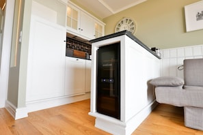 A modern kitchen with white cabinetry, a built-in oven, and a grey armchair in the living area.