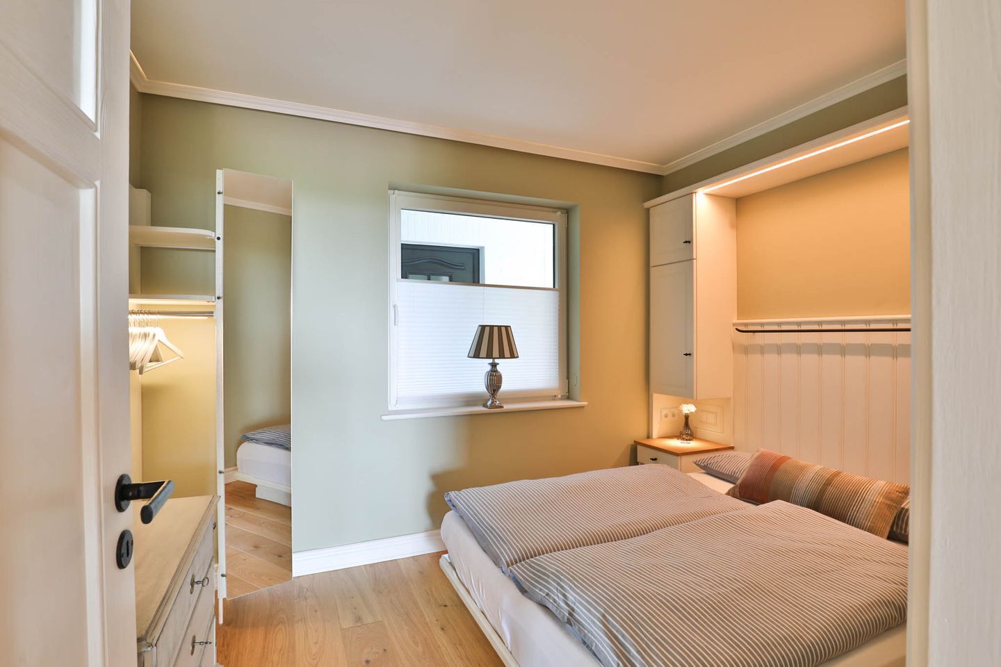 Ein Schlafzimmer mit Bett, Nachttisch, Lampe, Fenster und Kleiderschrank.