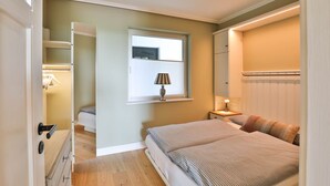 Ein Schlafzimmer mit Bett, Nachttisch, Lampe, Fenster und Kleiderschrank.