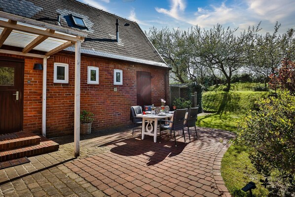 Une maison en briques avec un patio couvert, une table et des chaises, et un jardin.