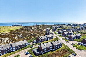 A coastal residential area with houses, a road, and a bridge in the background.