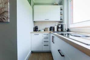 A modern kitchen with white cabinets, a wooden countertop, and a window providing natural light.