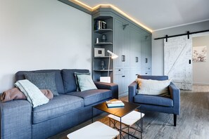 Ein modernes Wohnzimmer mit einem grauen Sofa, einem blauen Sessel, einem Couchtisch und einer eingebauten Bücherwand mit Büchern und Dekoration.