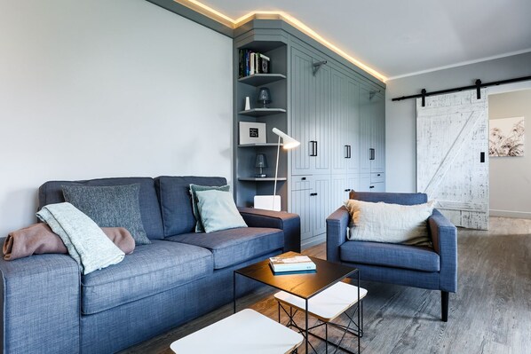 A modern living room with a grey sofa, a blue armchair, a coffee table, and a built-in shelving unit with books and decorative items.