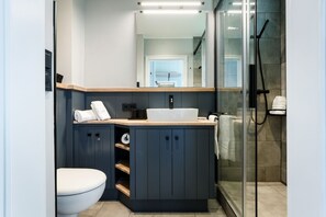 Un baño moderno con tocador azul oscuro, inodoro blanco y cabina de ducha de vidrio.