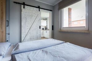 A bedroom with a bed, a sliding barn door, a window, and a view of a kitchen.