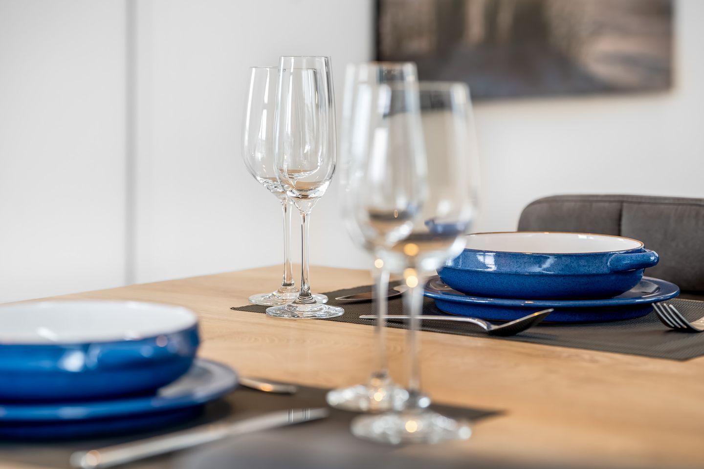 Une table à manger dressée avec des assiettes bleues, des verres à vin transparents et des couverts.