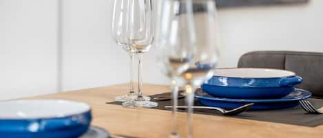 Une table à manger dressée avec des assiettes bleues, des verres à vin transparents et des couverts.