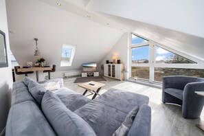 Un loft modern amb un sostre alt, una zona de menjador, un saló amb un sofà gris i una finestra gran que ofereix vistes a l'exterior.
