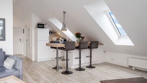 A modern kitchen with a dining area, featuring a skylight, white cabinetry, and a wooden dining table with bar stools. - Frisch Sanierte Wohnung in Ruhiger, Strandnaher Lage von Hörnum. - Berliner Ring (Hörnum (Sylt))
