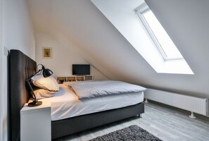 A bedroom with a sloped ceiling, a bed, a desk, a chair, a TV, and a window. - Frisch Sanierte Wohnung in Ruhiger, Strandnaher Lage von Hörnum. - Berliner Ring (Hörnum (Sylt))