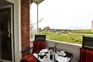 A balcony with a table set for two, overlooking a grassy area with houses in the background.