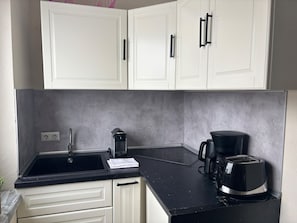 Eine Küche mit weißen Schränken, einer schwarzen Arbeitsplatte, einem Spülbecken, einer Kaffeemaschine und einem Toaster.