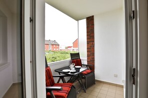 Un balcón con mesa y sillas, un muro de ladrillo y vistas a edificios residenciales.