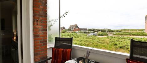 A balcony with a table set for two, overlooking a grassy area with houses in the background.
