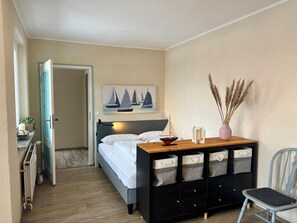 Un dormitorio con cama, escritorio con espacio de almacenamiento, silla, radiador y puerta.