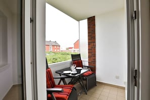 A balcony with a table and chairs, a brick wall, and a view of residential buildings.