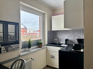 A compact kitchen with a window, a radiator, a sink, a coffee maker, and a cabinet.