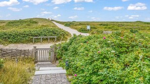 A pathway leading through a lush, green landscape with a wooden gate and a signboard. - Beach house - Fantastic detached house under thatch - in the immediate vicinity of the beach. (Hörnum (Sylt))