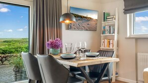 A dining area with a table set for two, a vase of flowers, and a bookshelf with books. - Beach house - Fantastic detached house under thatch - in the immediate vicinity of the beach. (Hörnum (Sylt))