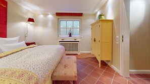 A bedroom with a bed, a bench, a window, a radiator, and a yellow cabinet.