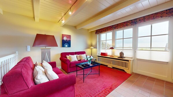 A living room with a red sofa, a coffee table, and a window with blinds.
