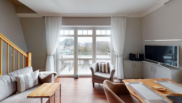 A modern living room with a sofa, armchair, wooden coffee table, and a TV on a stand.