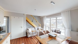 A modern living room with a wooden staircase, a dining table, and a sofa.