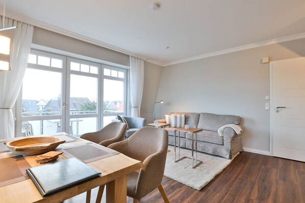 A modern living room with a sofa, chairs, a dining table, and a large window.