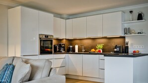 A modern kitchen with white cabinetry, a built-in oven, a coffee station, and a small island with fruits and vegetables. - Lornsendüne - Modern apartment in an absolutely beachfront location in Westerland with (Sylt)