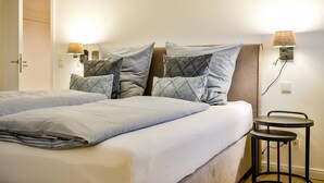 A double bed with a light blue bedspread and multiple pillows, a bedside table with a lamp, and a chair. - Lornsendüne - Modern apartment in an absolutely beachfront location in Westerland with (Sylt)