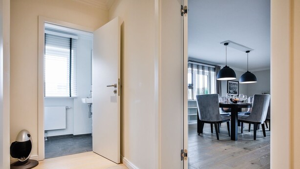 A modern kitchen with white cabinets, a dining area with a table and chairs, and a view of the outside through a window. - Lornsendüne - Modern apartment in an absolutely beachfront location in Westerland with (Sylt)